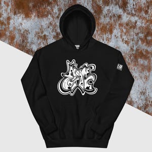 以下が含まれることがあります： グラフィティスタイルのフォントで「Stay」という言葉が白で書かれた黒いフード付きスウェットシャツです。