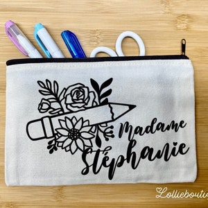 May include: A white canvas zippered pouch with a black pencil and floral design. The text "Madame Stéphanie" is printed on the pouch.