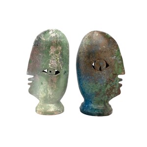 Puede incluir: Dos esculturas de cerámica de rostros abstractos en colores verde, azul y marrón. Las esculturas son estilizadas y tienen un diseño simple y moderno.