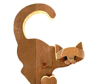 Può includere: Una statuetta di gatto in legno con finitura marrone. Il gatto è seduto con la coda arrotolata dietro la schiena. Gli occhi del gatto sono dipinti di nero.