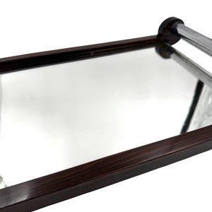 Puede incluir: Una bandeja rectangular con superficie de espejo y marco de madera marr&oacute;n oscuro. La bandeja tiene un asa cromada y est&aacute; inclinada hacia el espectador, mostrando sus cualidades reflectantes.