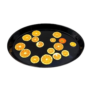 May include: A black oval serving tray with a decorative design of orange slices. The tray is perfect for serving snacks, drinks, or appetizers.