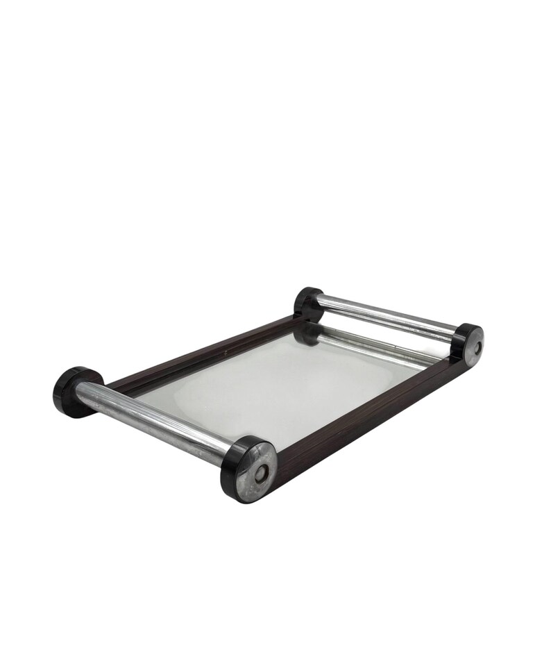 Puede incluir: Una bandeja rectangular con superficie de espejo y marco de madera marr&oacute;n oscuro. Cuenta con dos asas cil&iacute;ndricas de color plateado con detalles negros en cada extremo. La bandeja est&aacute; dise&ntilde;ada para servir alimentos o bebidas.