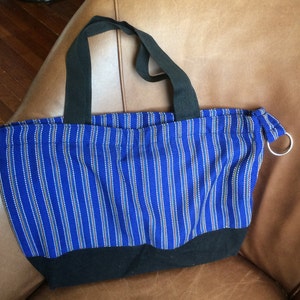 May include: A blue and black striped tote bag with black handles. The bag has a black bottom and a silver ring on the side.