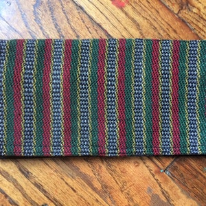 May include: A striped fabric wallet with red, green, yellow, and blue stripes. The wallet is made of a woven fabric and has a dark brown leather trim.