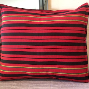 May include: Red and black striped pillow with green and yellow accents. The pillow is made of a woven fabric and has a square shape.