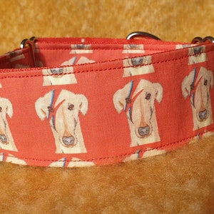 May include: A red dog collar with a repeating pattern of white dogs with black markings. The collar has silver hardware.