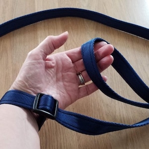 May include: A dark blue adjustable wrist strap with a black buckle. The strap is made of a thick, woven material.