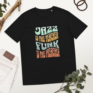 Może przedstawiać: Czarny T-shirt z grafiką w stylu retro, na której widnieje napis "Jazz is the teacher Funk is the preacher".
