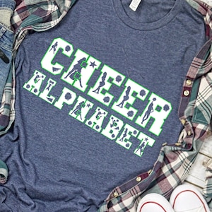 Puede incluir: Una camiseta azul marino con el texto "Cheer Alphabet" en letras blancas con contorno verde. Las letras est&aacute;n decoradas con siluetas de animadoras en varias poses.