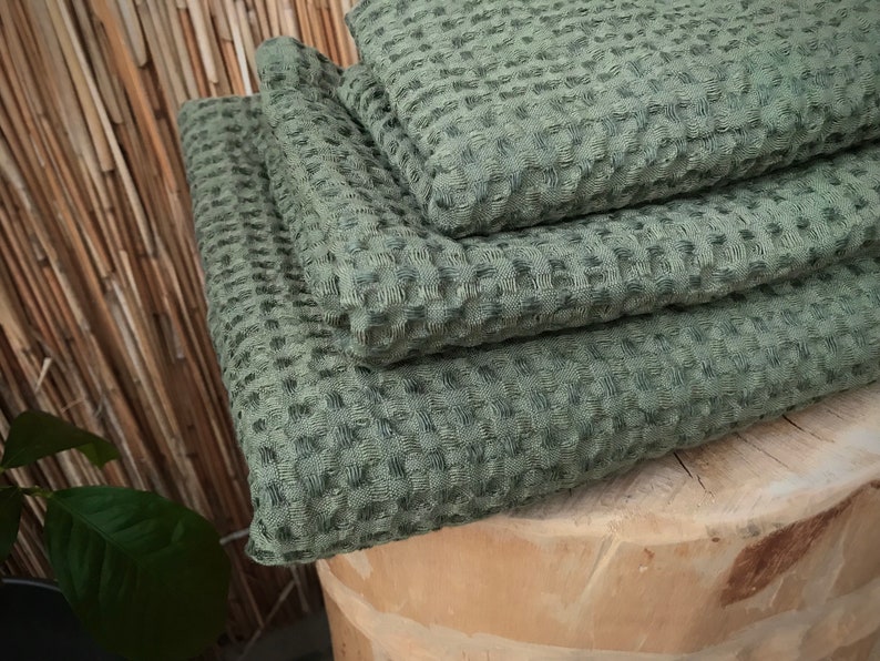 May include: A stack of four green waffle weave towels folded on a wooden surface.
