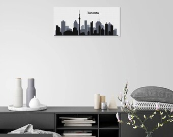 May include: A framed print featuring a grayscale silhouette of the Toronto skyline. The print displays the city's iconic buildings and the CN Tower, with the word "Toronto" above the skyline. The artwork is displayed on a white wall above a dark gray cabinet.
