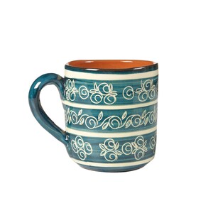 Pode incluir: Uma caneca de cerâmica azul com desenhos florais brancos e uma borda marrom.