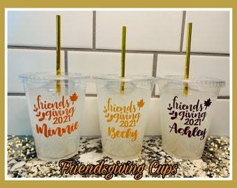May include: Three clear plastic cups with gold straws and personalized labels that say "Friendsgiving 2021" with a name on each cup. The names are Minnie, Becky, and Ashley. The cups are sitting on a gold glitter surface.