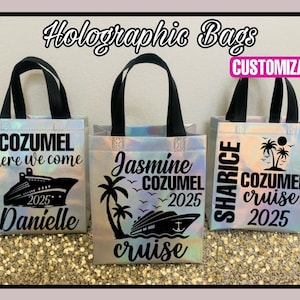 Pode incluir: Tr&ecirc;s sacolas de m&atilde;o hologr&aacute;ficas iridescentes com al&ccedil;as pretas e texto preto. As sacolas s&atilde;o personalizadas com o texto "Cozumel here we come 2025 Danielle", "Jasmine Cozumel 2025 cruise" e "Sharice Cozumel cruise 2025".