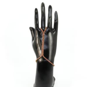 May include: A gold-tone finger and wrist bracelet with pink rhinestones. The bracelet is worn on a black mannequin hand.