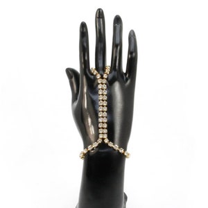 May include: A gold-tone finger and wrist chain bracelet with clear rhinestones. The bracelet is designed to wrap around the finger and wrist, creating a unique and stylish look.
