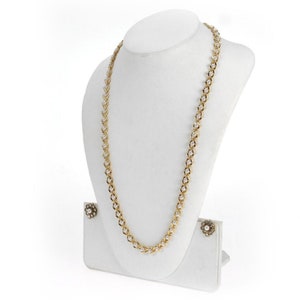 May include: A gold chain necklace with white pearl-like beads and matching earrings. The necklace is displayed on a white velvet bust form.