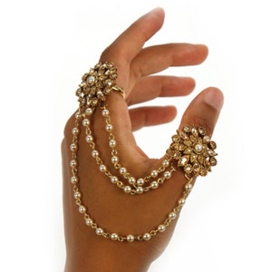 May include: A gold ring with a pearl and crystal flower design, connected to a thumb ring with a similar design by a chain of pearls.