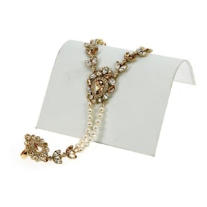 May include: A gold-tone bracelet with a pearl and crystal design. The bracelet has a ring attached to one end and a teardrop-shaped pendant with a crystal in the center.