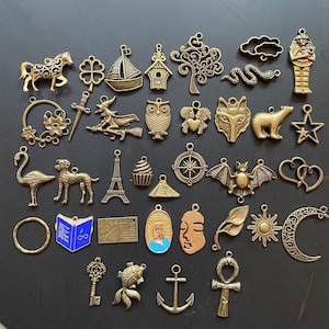 Könnte beinhalten: Eine Sammlung von 35 verschiedenen Metall-Anhängern mit verschiedenen Designs, darunter Tiere, Gegenstände und Symbole. Die Anhänger sind bronzefarben und haben eine Vintage-Ästhetik.
