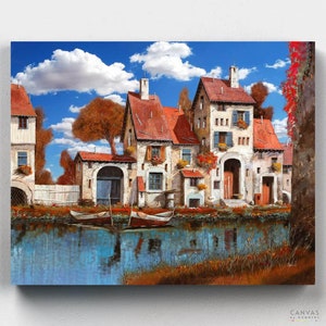 May include: A painting of a quaint village with colorful houses lining a canal. The houses have red tile roofs and white walls, with windows and doors. There are trees and flowers in the foreground, and a blue sky with white clouds in the background. Two boats are docked in the canal.