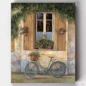 May include: A vintage-style bicycle with a wicker basket filled with red flowers is parked in front of a building with a window and shutters. The window is decorated with potted plants and has a view of a lush green garden.