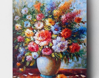 May include: A colorful bouquet of flowers in a white vase with a blue rim. The flowers are arranged in a vase on a red and brown surface. The flowers include roses, daisies, and other blooms in shades of pink, red, white, yellow, and blue.