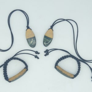 May include: Two black cord necklaces with wooden pendants. The pendants are oval shaped and have a green and brown marbled design. Two black cord bracelets with wooden bar pendants. The pendants are rectangular and have a green and brown marbled design.