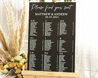 May include: A black chalkboard easel sign with white text that reads "Please find your seat" and "Matthew & Andrew 06.05.2023". The sign lists guest names alphabetically by table.