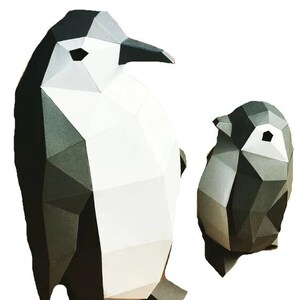 May include: Two origami penguins, one large and one small, made of white and gray paper. The larger penguin is standing upright with its wings folded, while the smaller penguin is sitting with its wings spread out.