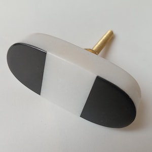 May include: White and black oval cabinet knob with a gold screw. The knob has a geometric pattern of black and white stripes.