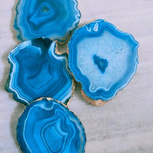May include: Four blue agate coasters with gold trim. The coasters are round and have a natural, organic look.