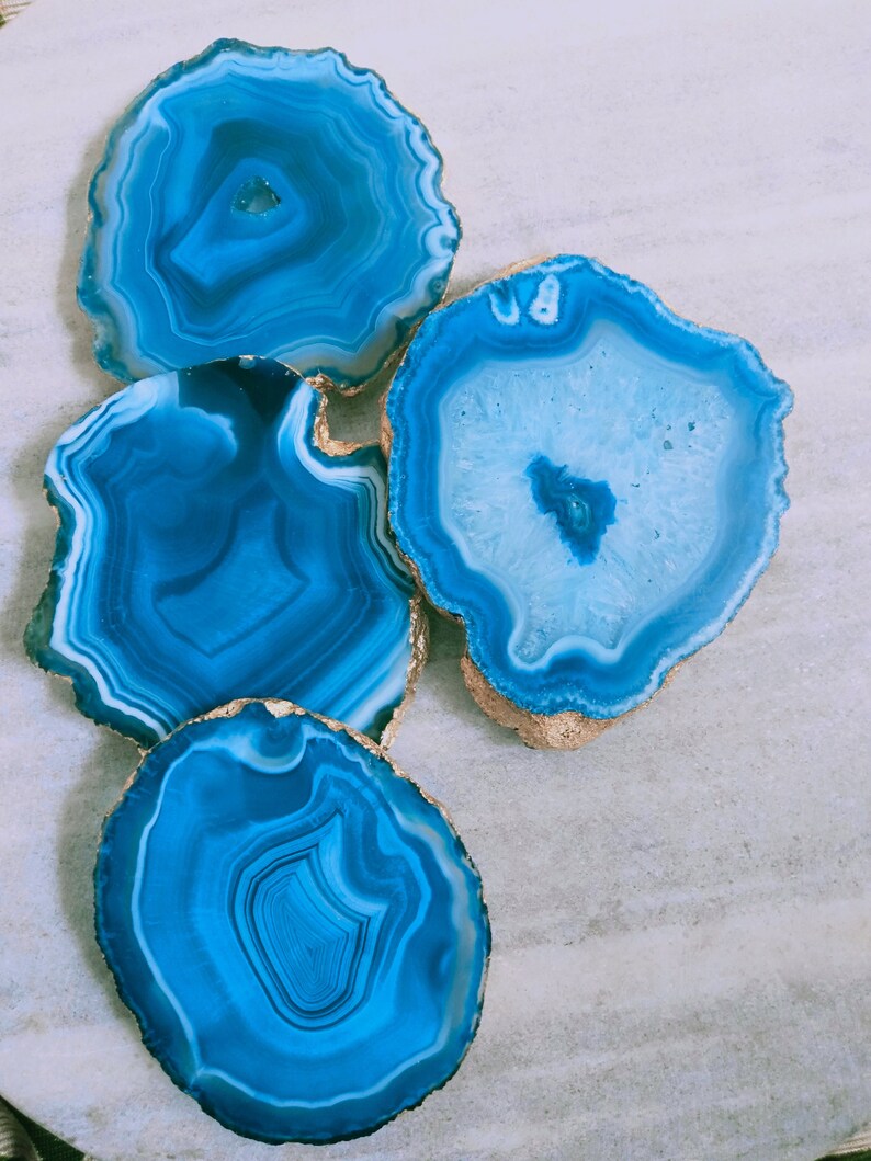 May include: Four blue agate coasters with gold trim. The coasters are round and have a natural, organic look.