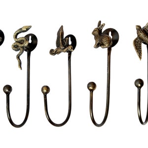 Op de afbeelding: Vijf decoratieve haken met dierlijke eindstukken. De haken zijn gemaakt van metaal en hebben een donker bronzen afwerking. De eindstukken zijn een bij, een slang, een vogel, een konijn en een zwaluw.