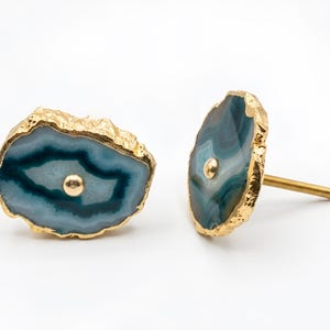 May include: Two cabinet knobs featuring polished, irregular slices of blue and white agate stone. Each slice is edged in a textured gold-tone metal finish and features a central gold-tone metal stud. One knob is shown from the front, and one from the side.