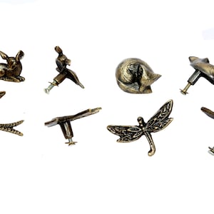 Puede incluir: Surtido de pomos de armario de color dorado antiguo con varios diseños de animales e insectos, incluyendo un ciervo, un conejo, un zorro, una libélula, una mariposa y una golondrina.