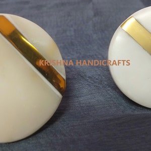May include: Two white round knobs with a gold stripe across the centre. The knobs are made of bone and have a polished finish.  KRISHNA HANDICRAFTS is printed on the image.