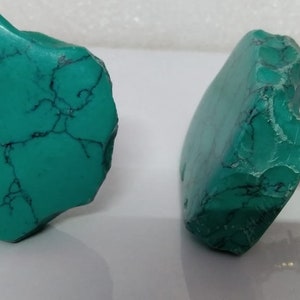 Może przedstawiać: Dwa turkusowe zielone kamienne gałki do szafek z mosiężną śrubą. Gałki mają nieregularny kształt i szorstką, naturalną fakturę.