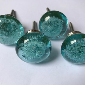 May include: Four round, light blue glass cabinet knobs with a bubble-like design inside. Each knob has a silver-colored metal stem for mounting. The knobs are a decorative hardware item.