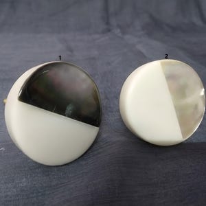 Può includere: Due pomelli rotondi per armadi etichettati 1 e 2. Il pomello 1 presenta un design diviso con una metà superiore grigio antracite iridescente scuro e una metà inferiore bianco opaco. Il pomello 2 ha un design diviso con parte superiore madreperlacea e base bianco opaco.