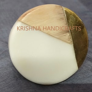 May include: A round cabinet knob with a segmented design. The knob features a white, light wood, and gold-coloured metal finish. The text "KRISHNA HANDICRAFTS" is printed on the knob.