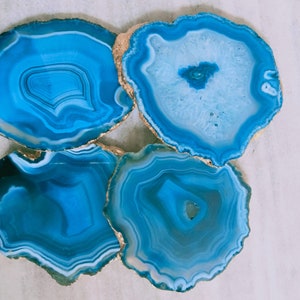 May include: Four blue agate coasters with gold trim. The coasters are round and have a natural, organic look.