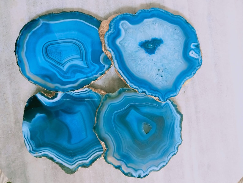 May include: Four blue agate coasters with gold trim. The coasters are round and have a natural, organic look.