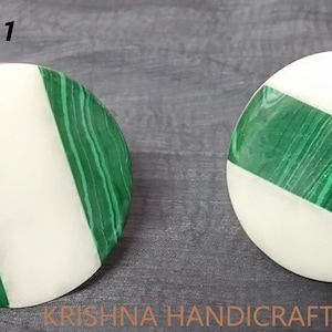 May include: Two round, white marble coasters with a green malachite stripe. The coasters are numbered 1 and 2.