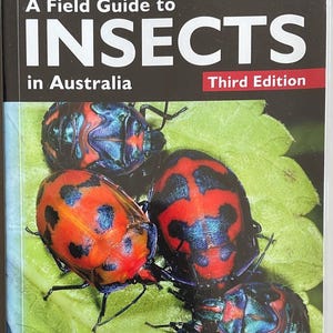 May include: A field guide to insects in Australia, third edition. The cover shows a close-up of several insects with red and black markings, set against a green leaf background. The insects have iridescent blue and black patterns.