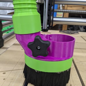 May include: A CNC router dust shoe in green, purple, and black. The dust shoe has a cylindrical top, a brush base, and a star-shaped knob. The brush base is black, and the other parts are green and purple.