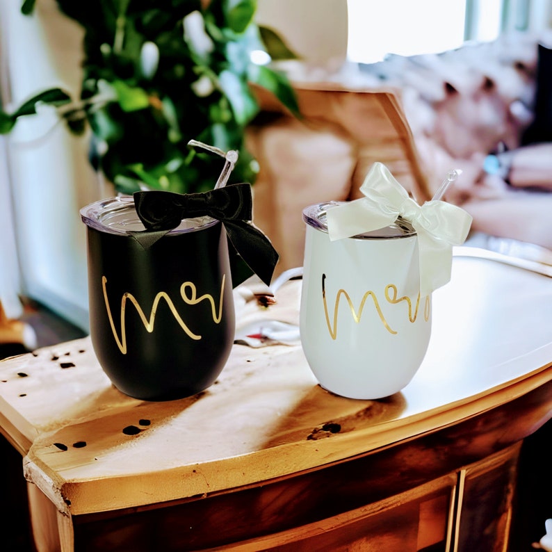 May include: Two stainless steel wine tumblers with lids and straws. One tumbler is black with a gold "Mr." inscription and a black bow. The other tumbler is white with a gold "Mrs." inscription and a white bow.