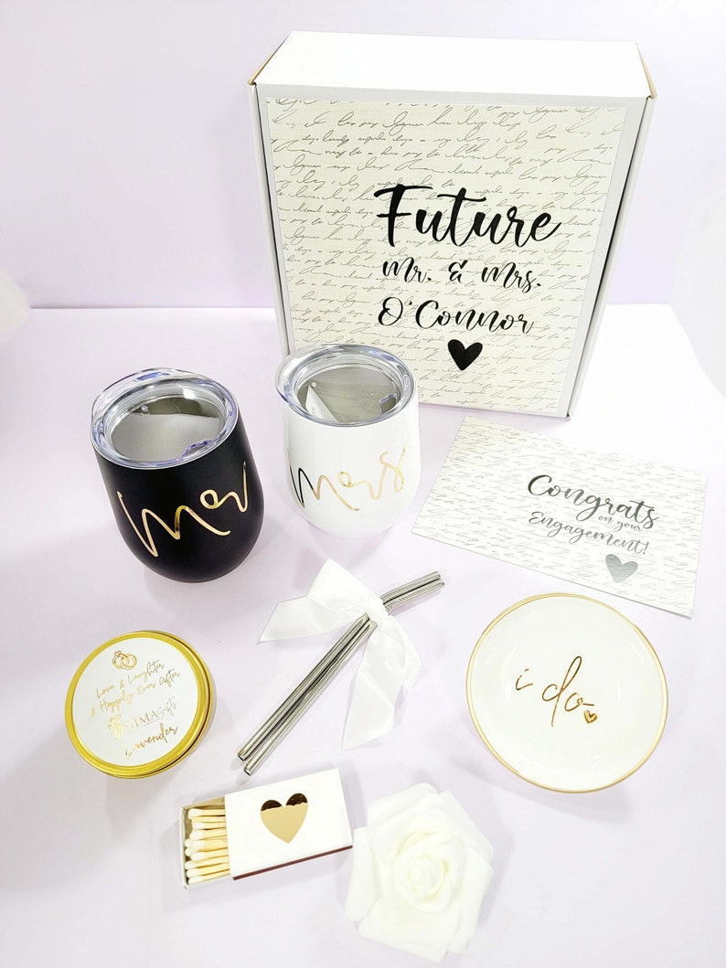 May include: A wedding gift set with a white box with the text "Future Mr. & Mrs. O'Connor" on it, two black and white tumblers, a white candle with the text "Love & Laughter Happily Ever After IMA of wonder", a white ring dish with the text "i do", a box of matches with a gold heart, a white rose, and a card with the text "Congrats on your Engagement!"