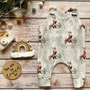 May include: A gray and white baby onesie with a fox print. The onesie has a fox, trees, butterflies, and moons on it. The onesie has a snap closure at the shoulders.